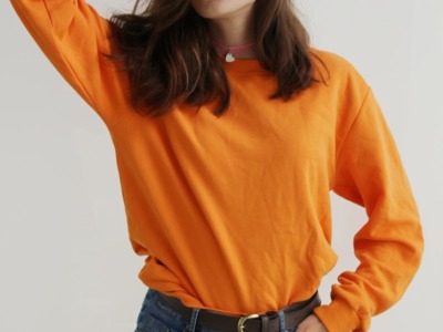 woman wearing orange crew-neck sweatshirt standing while putting right hand on her head